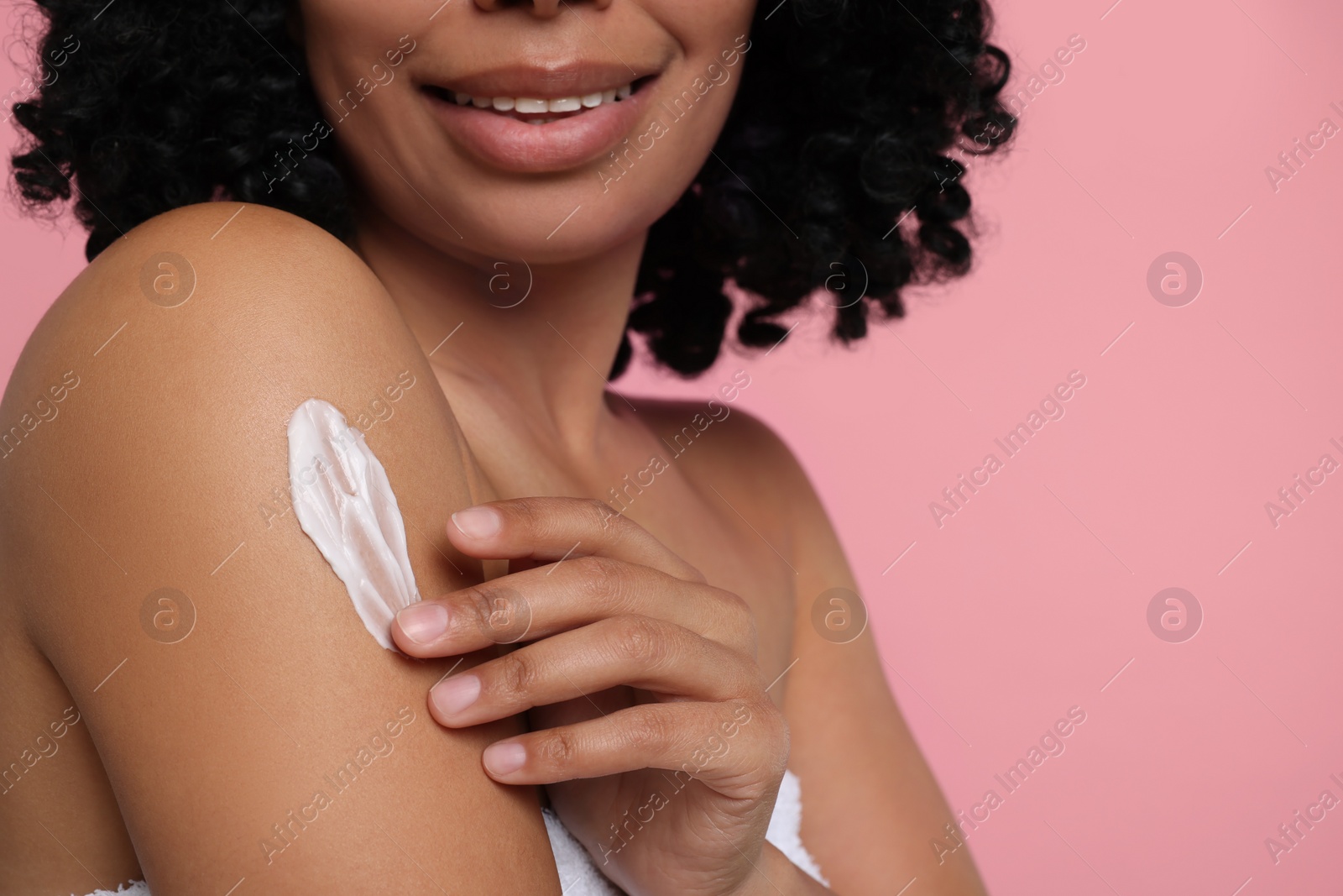 Photo of Young woman applying body cream onto shoulder on pink background, closeup