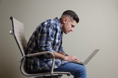 Man with poor posture using laptop while sitting on chair against grey background