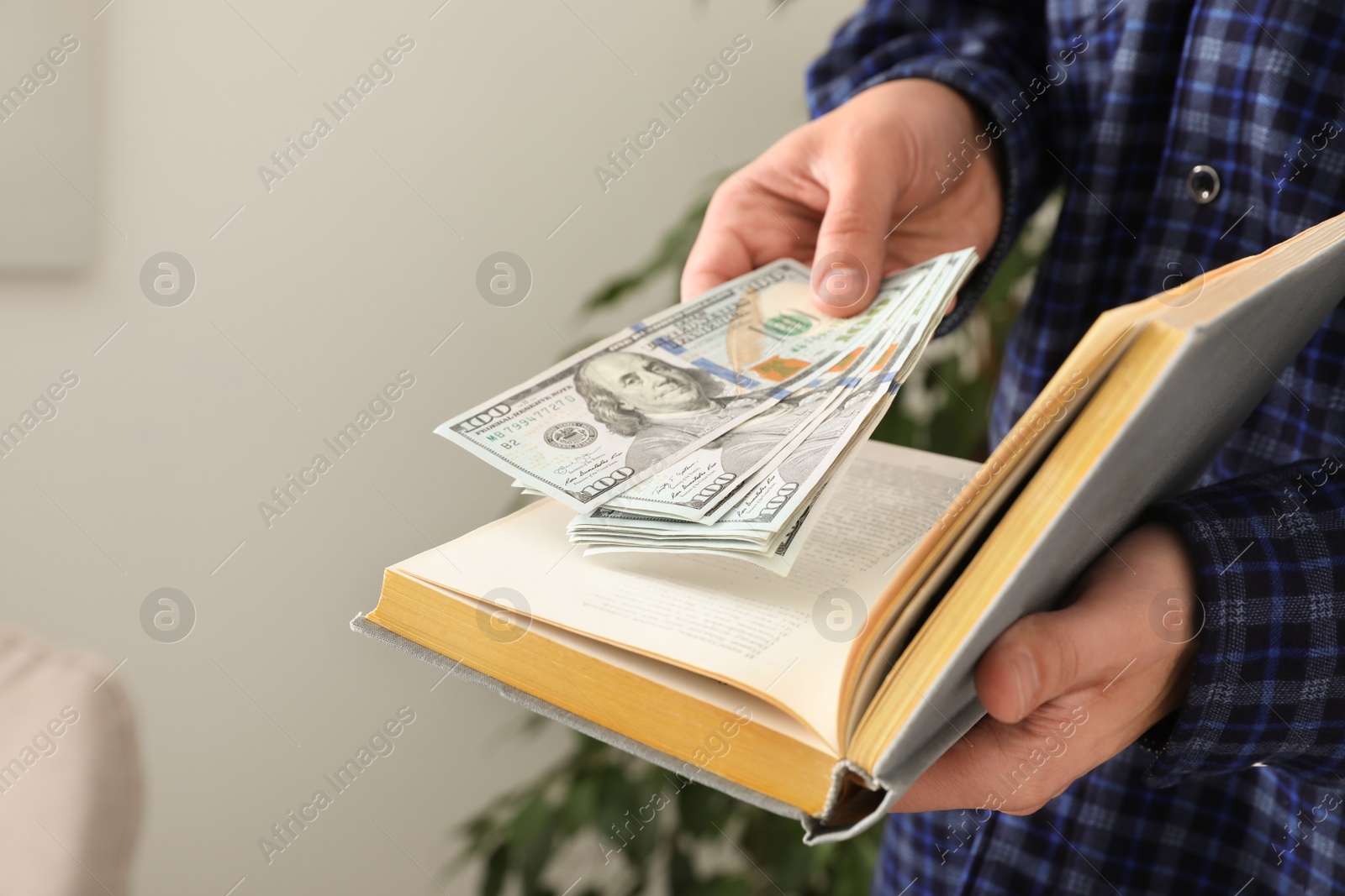 Photo of Man hiding dollar banknotes in book indoors, closeup. Money savings