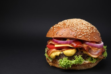 Delicious burger with bacon, patty and vegetables on black background. Space for text