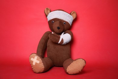 Toy bear with bandages on red background