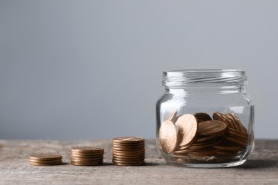 Photo of Glass jar with money and stack of coins on wooden table, closeup