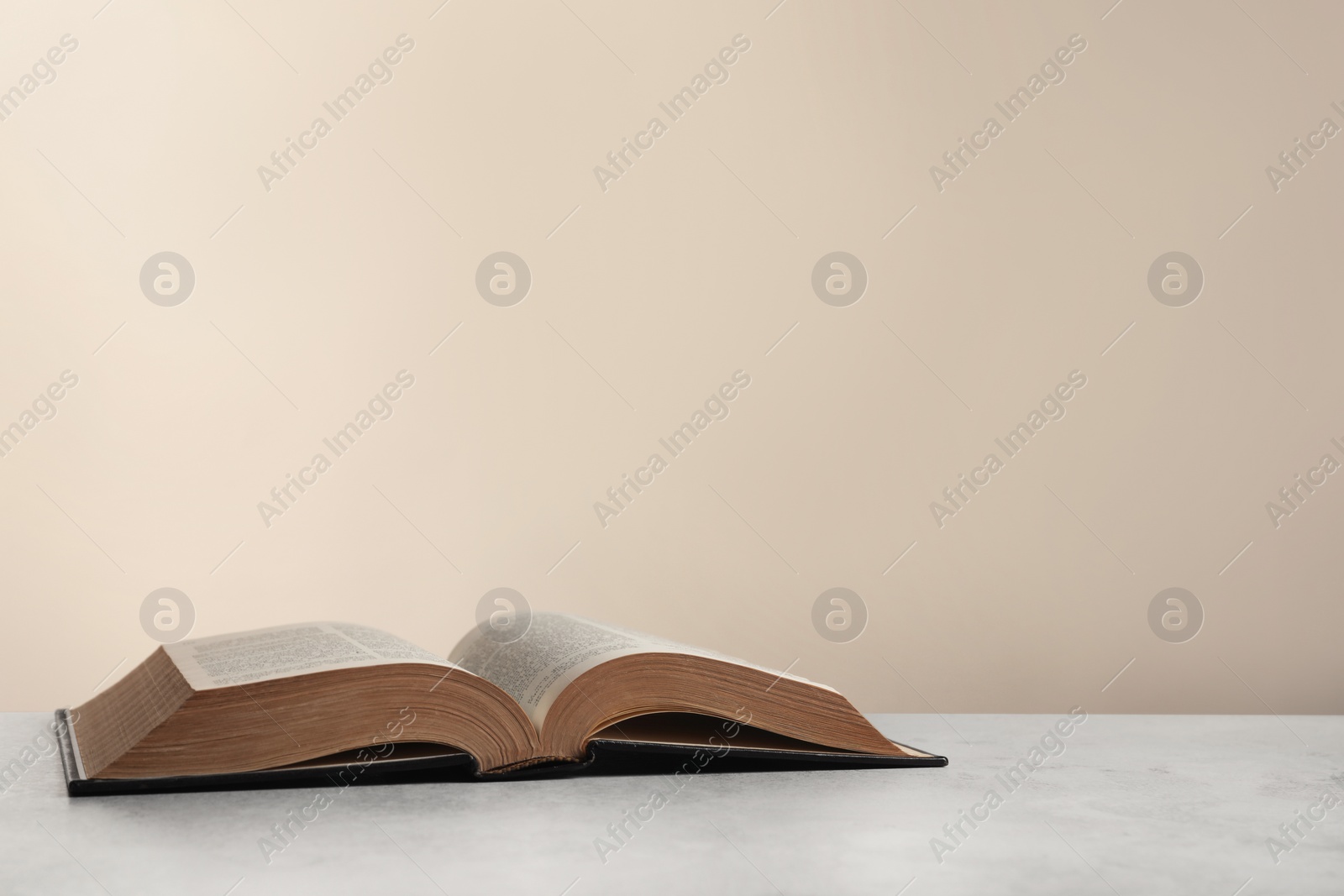 Photo of Open hardcover Bible on light grey table, space for text. Religious book