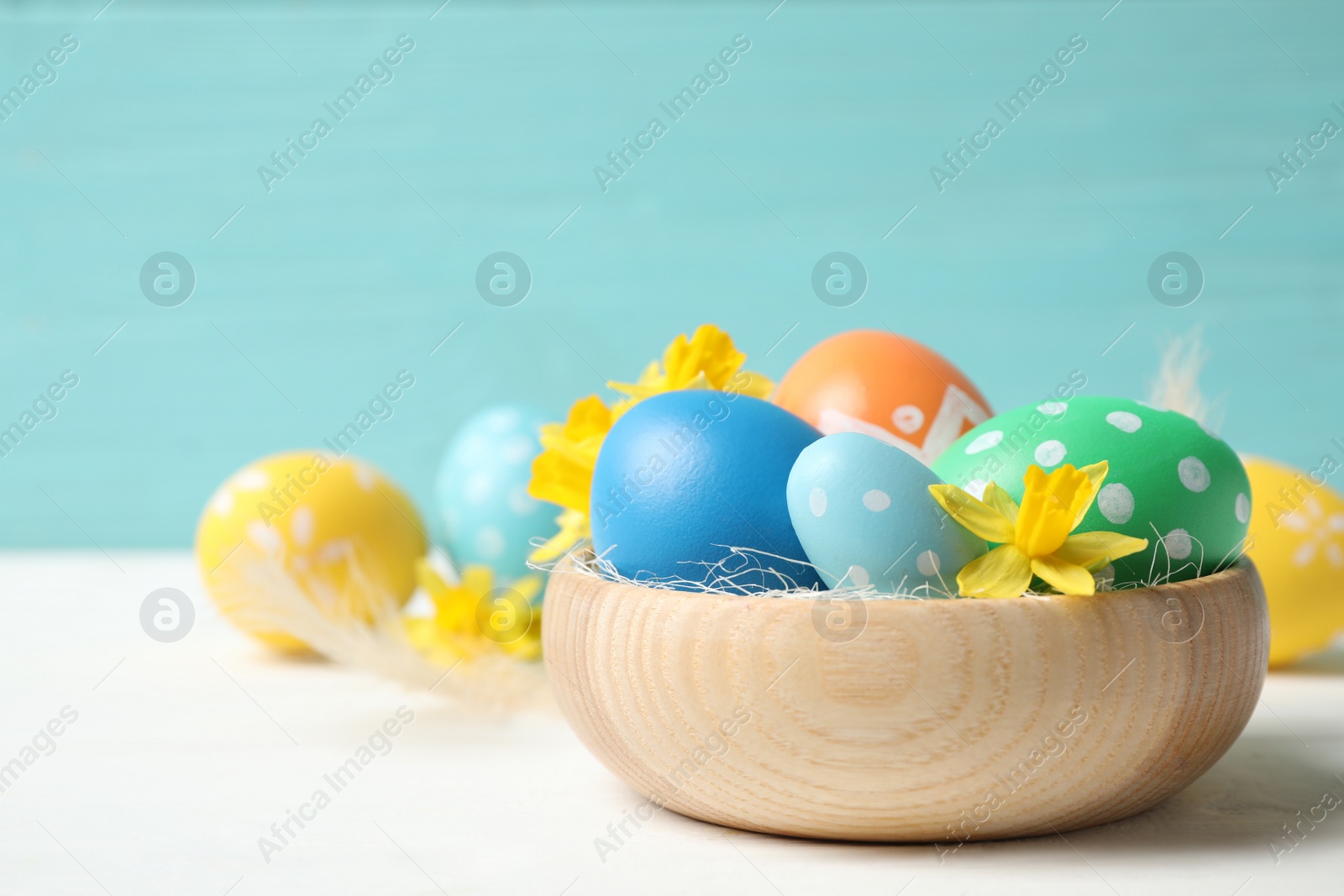 Photo of Colorful Easter eggs and flowers in bowl on white wooden table. Space for text