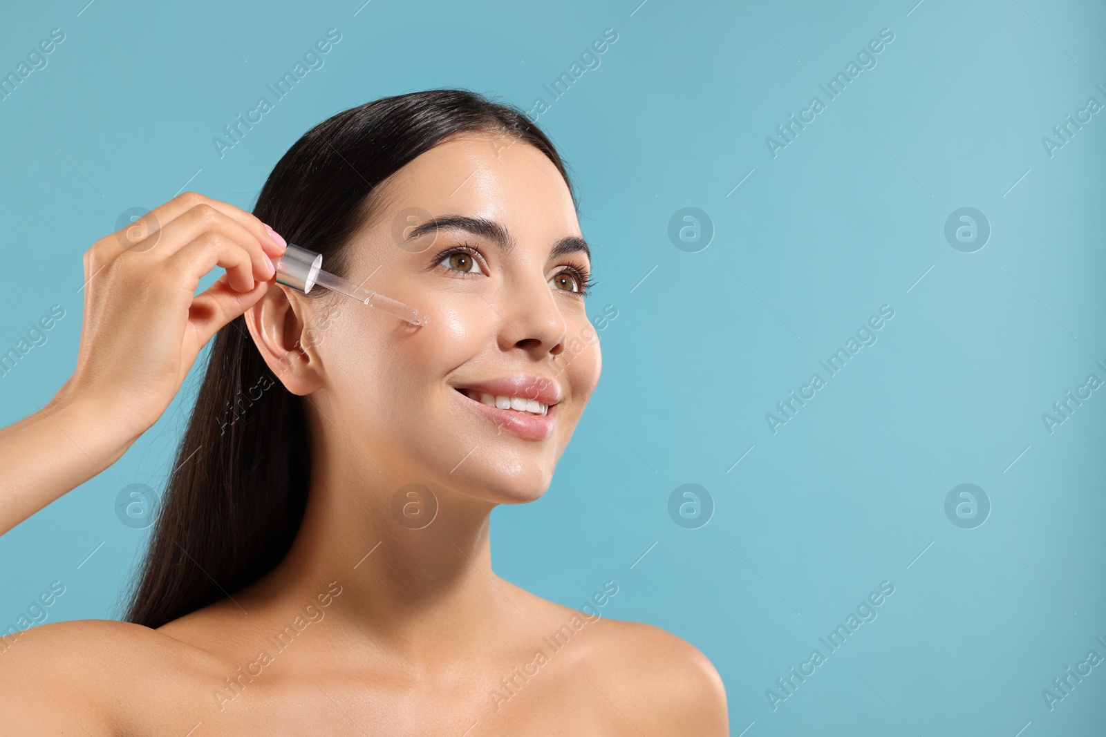 Photo of Beautiful young woman applying serum onto her face on light blue background. Space for text