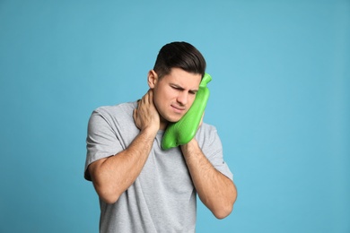 Photo of Man using hot water bottle to relieve neck pain on light blue background