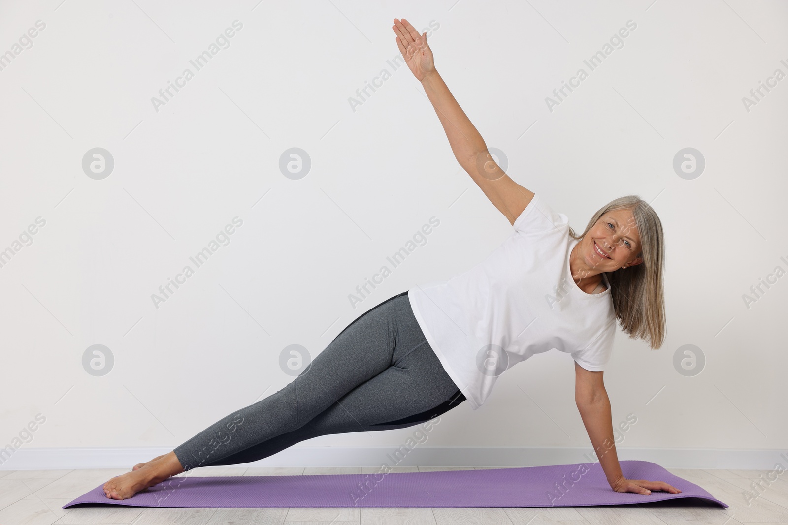 Photo of Happy senior woman practicing yoga on mat near white wall