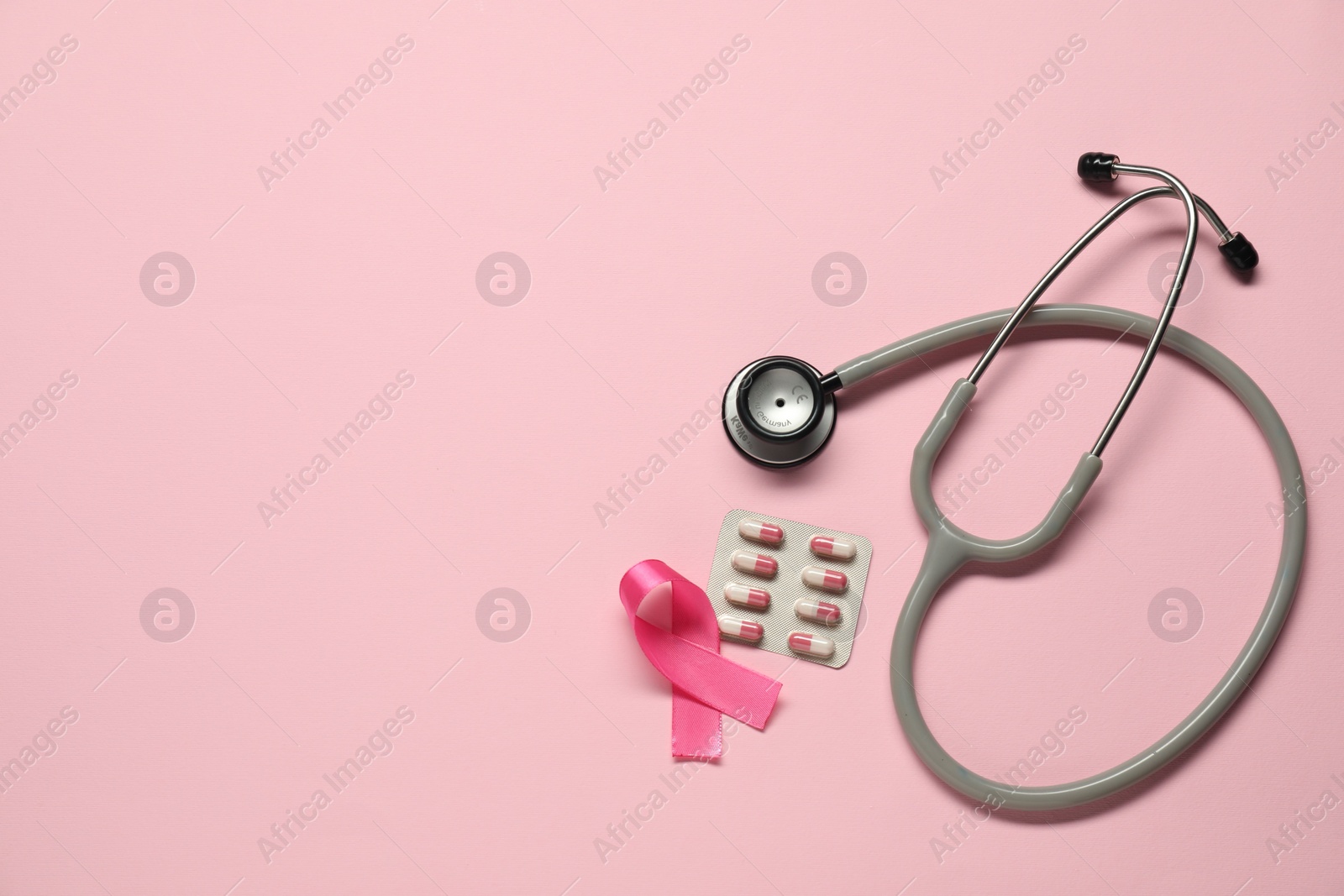 Photo of Breast cancer awareness. Pink ribbon, stethoscope and pills on color background, flat lay. Space for text