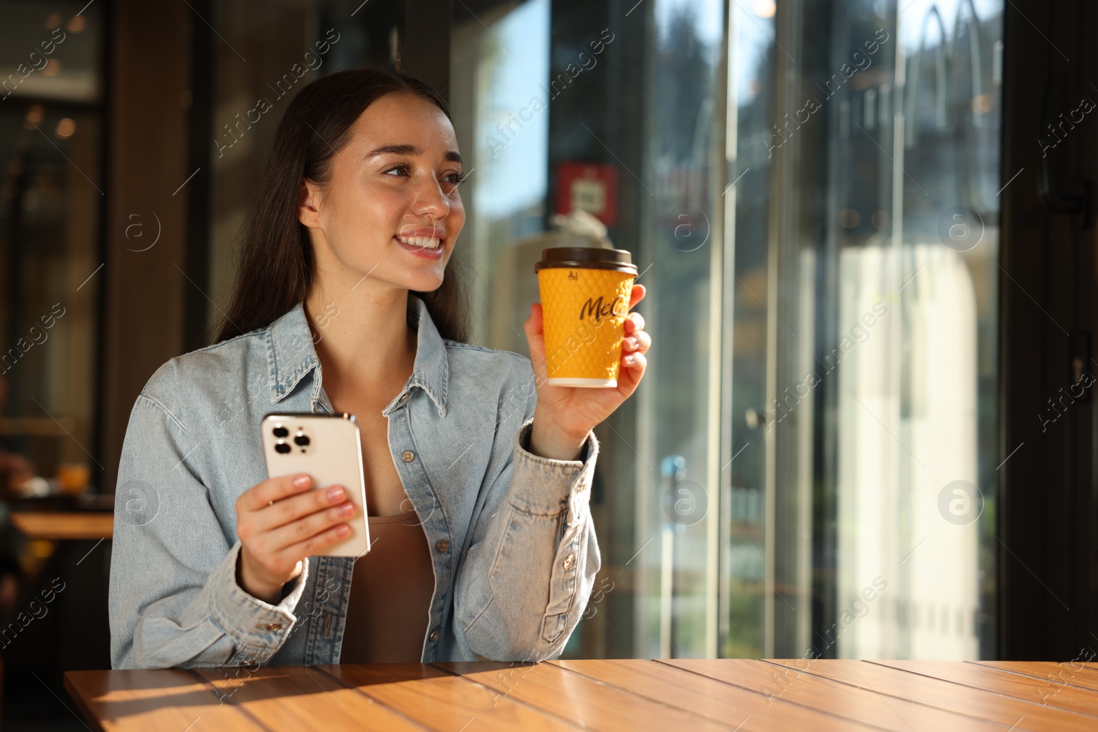 Photo of Lviv, Ukraine - September 26, 2023: Woman with hot McDonald's drink and smartphone at table in cafe, space for text