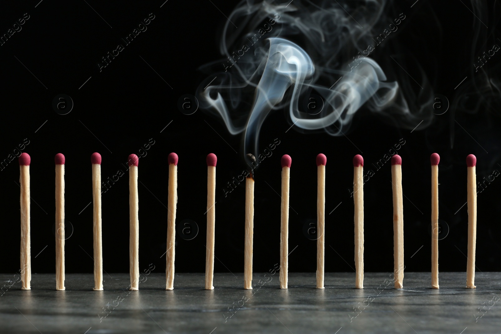 Photo of Burnt match among whole ones on table against black background