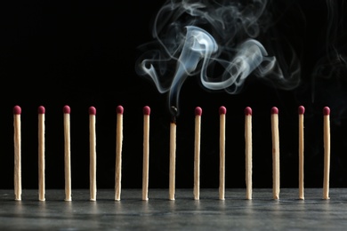 Photo of Burnt match among whole ones on table against black background