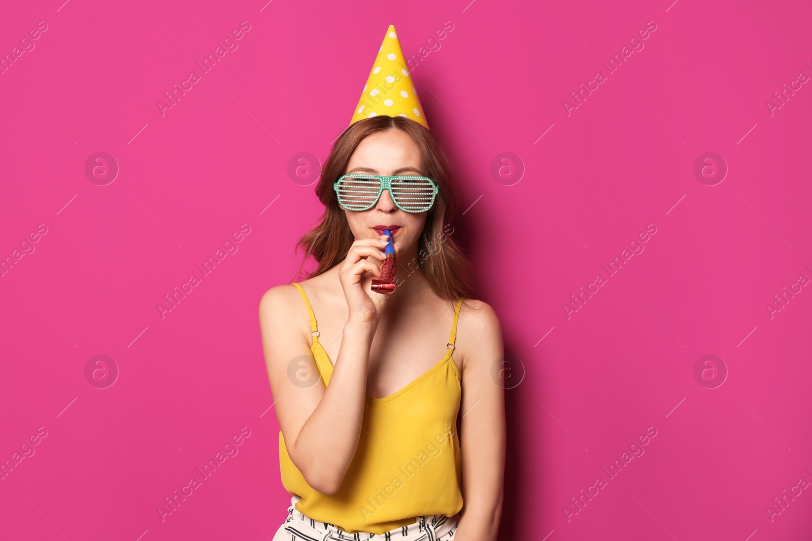 Photo of Young woman with party blower on color background. Birthday celebration