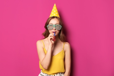 Photo of Young woman with party blower on color background. Birthday celebration