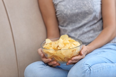 Photo of Woman with bowl of potato chips sitting on sofa, closeup