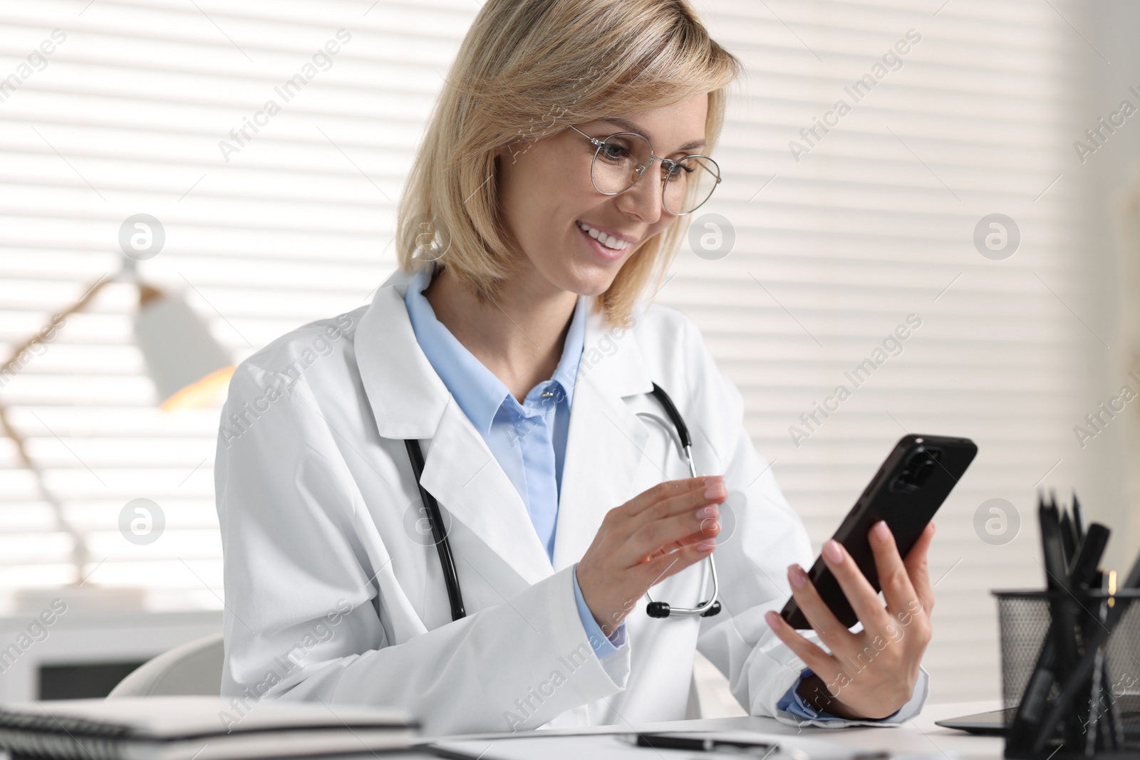 Photo of Smiling doctor with smartphone having online consultation in office