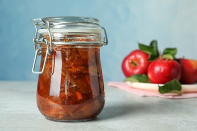 Photo of Tasty apple jam in glass jar and fresh fruits on light table, space for text