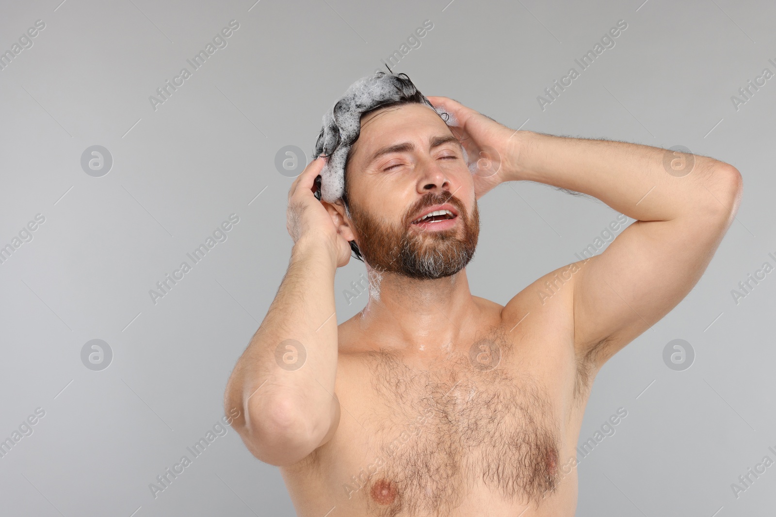 Photo of Handsome man washing his hair with shampoo on grey background. Space for text