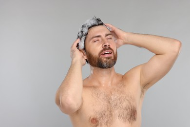 Handsome man washing his hair with shampoo on grey background. Space for text