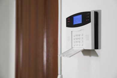 Home security alarm system on white wall near door, space for text