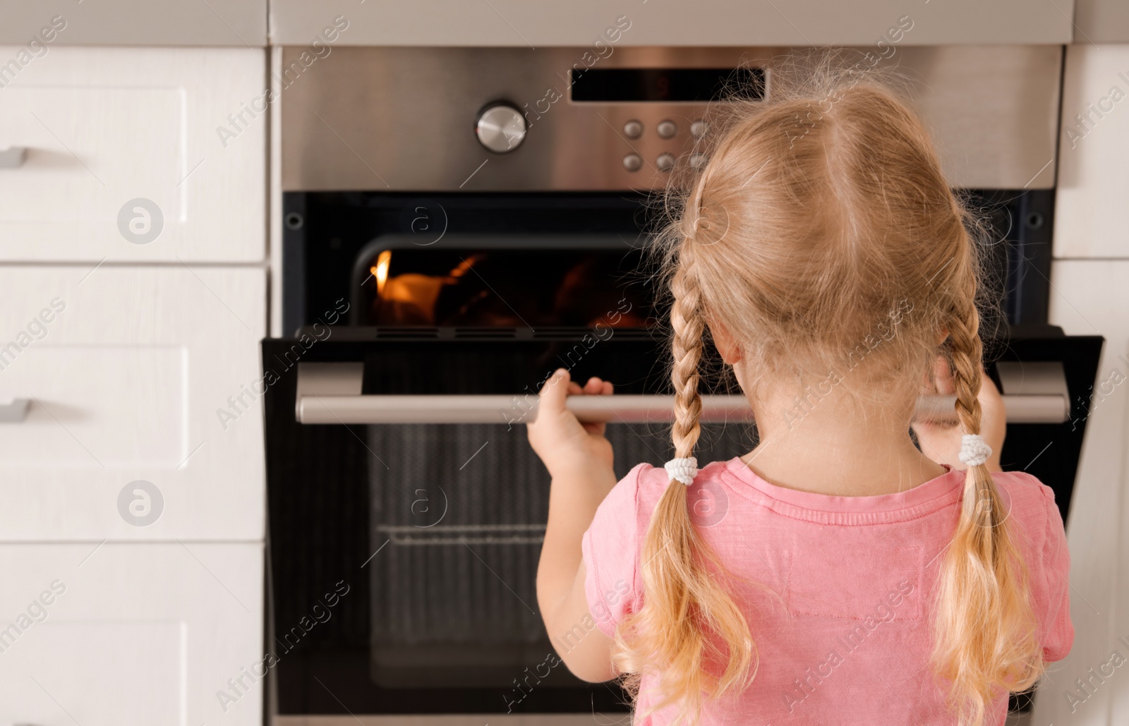 Photo of Little girl opening oven while baking in kitchen