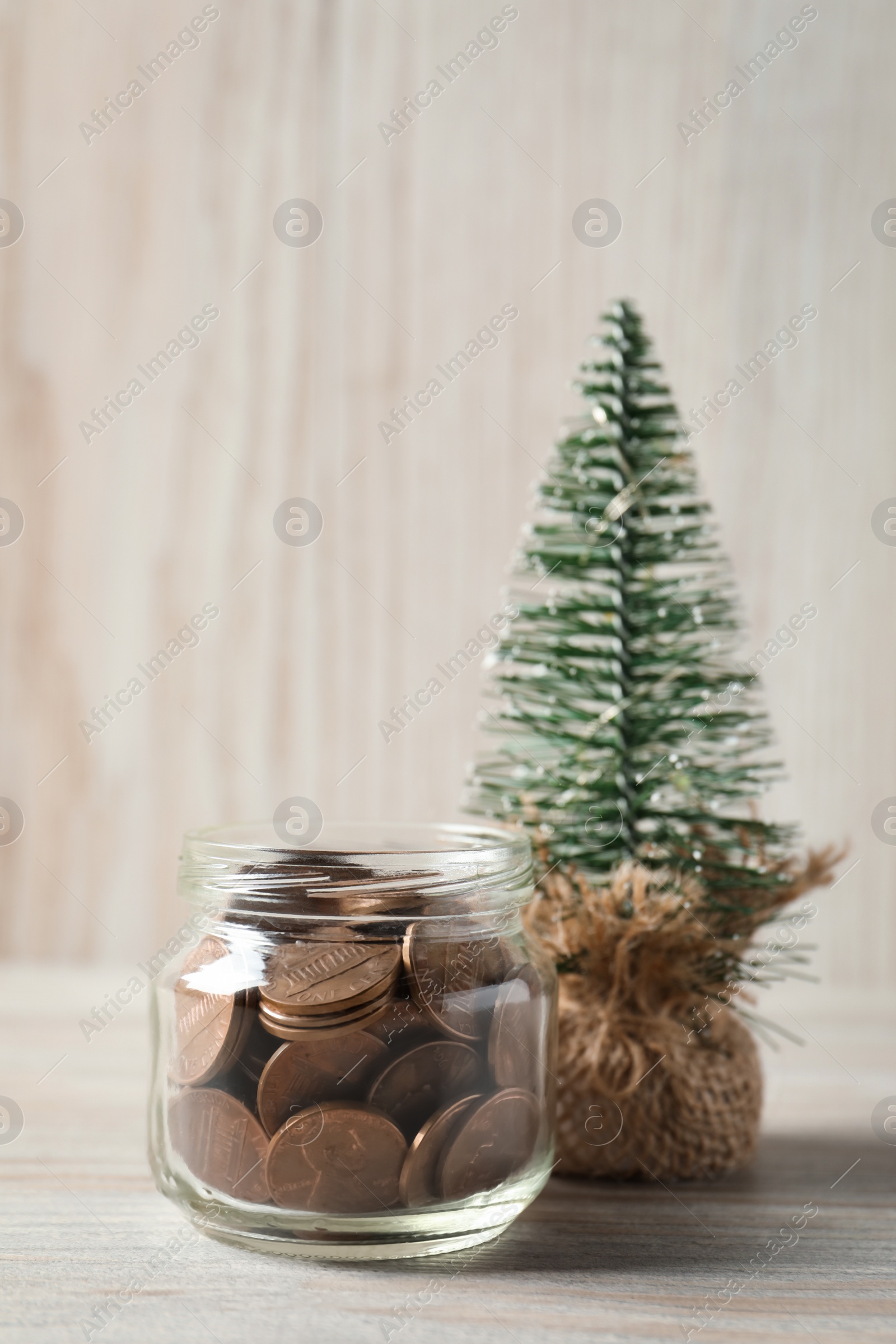 Photo of Glass jar with coins and small decorative tree on white wooden table, closeup