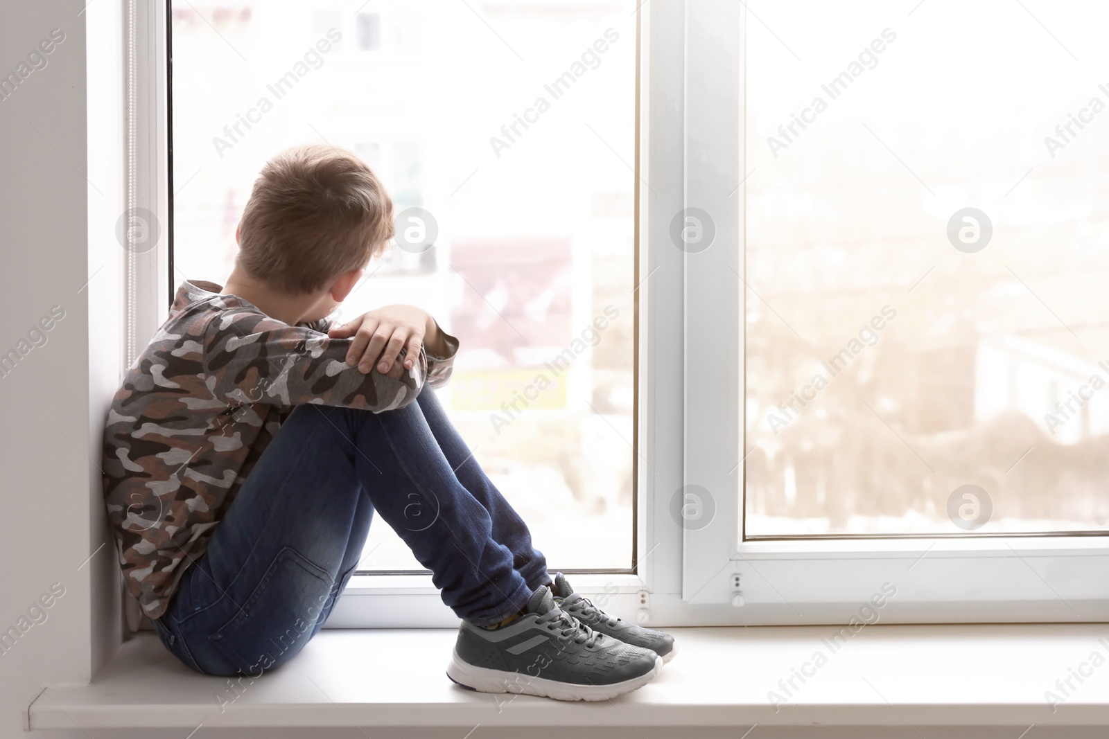 Photo of Lonely little boy near window indoors. Child autism