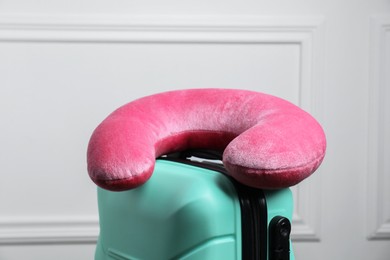 Photo of Pink travel pillow on turquoise suitcase near white wall