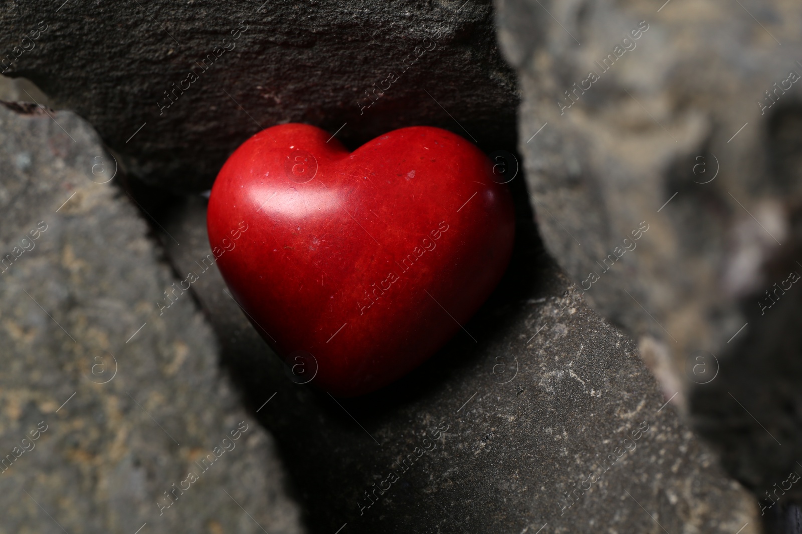 Photo of One red decorative heart between stones, closeup