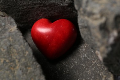 Photo of One red decorative heart between stones, closeup