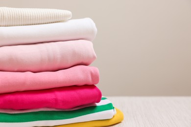 Photo of Stack of folded clothes on wooden table against grey background, closeup. Space for text