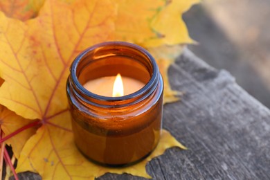 Burning candle and beautiful dry leaves on wooden surface outdoors, closeup with space for text. Autumn atmosphere