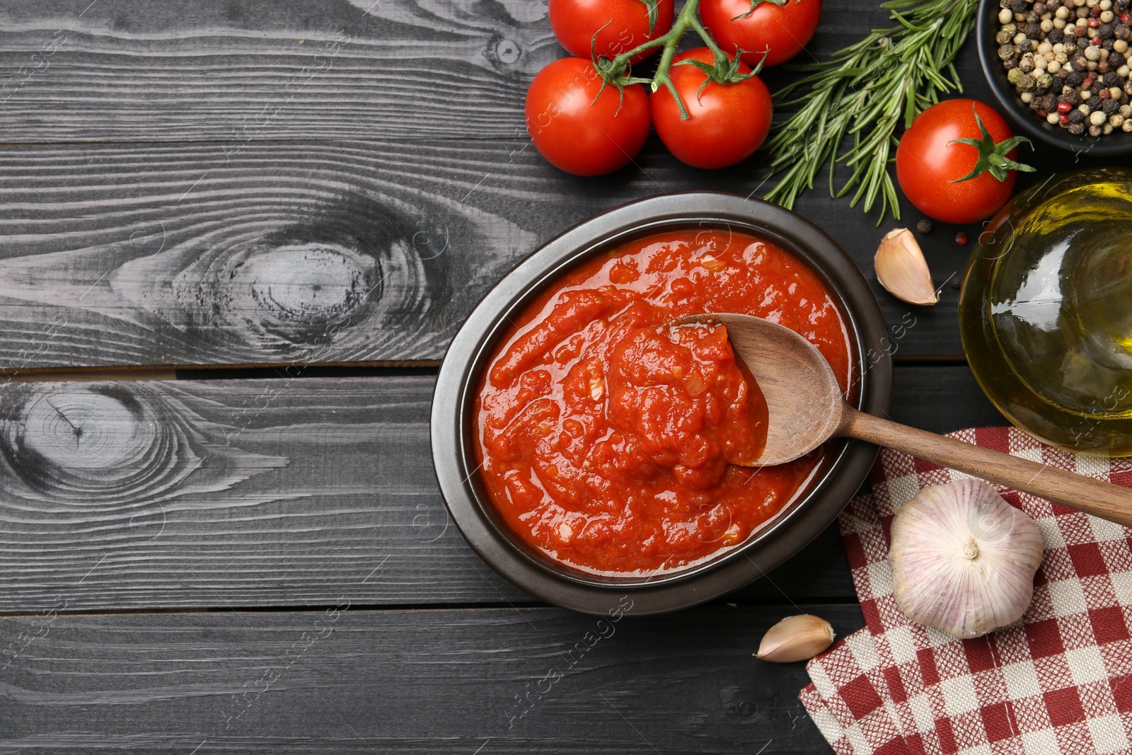 Photo of Homemade tomato sauce in bowl, spoon and fresh ingredients on black wooden table, flat lay. Space for text