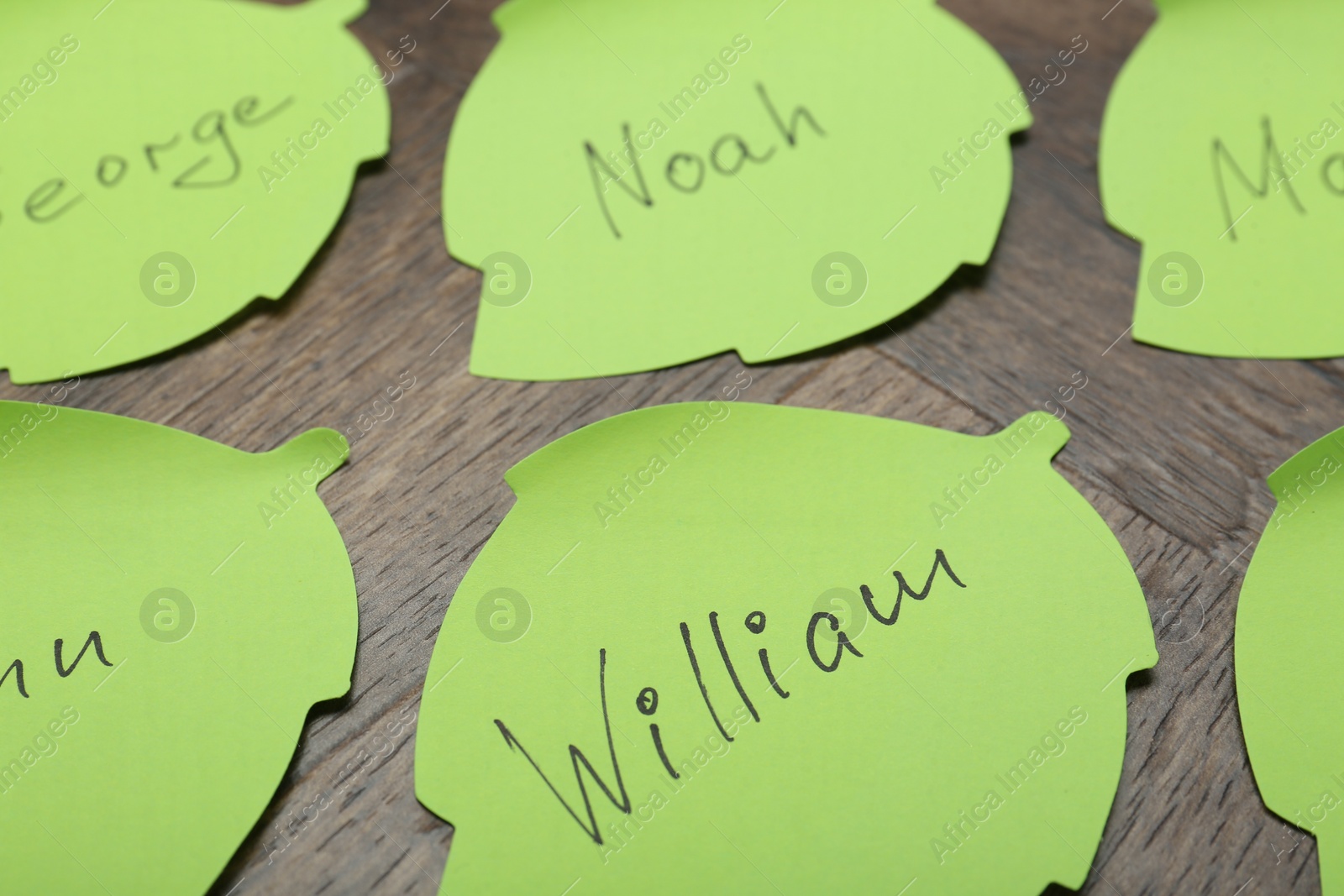 Photo of Paper stickers with different names on wooden table, closeup. Choosing baby's name