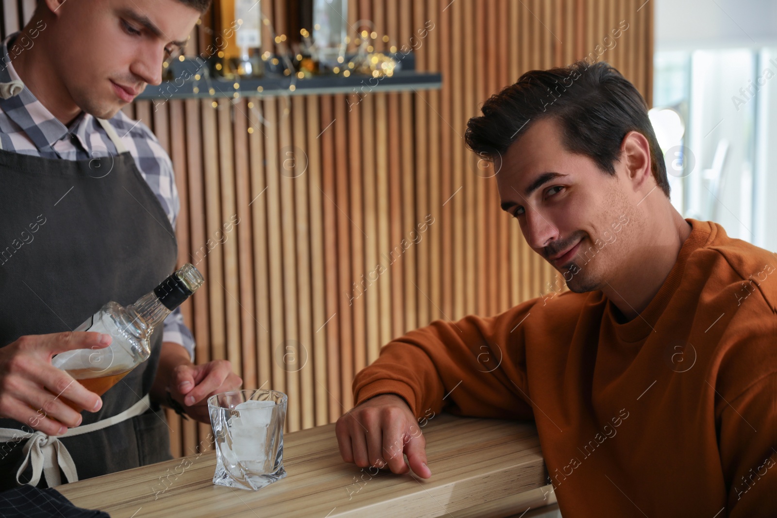 Photo of Bartender pouring whiskey for client at counter in pub