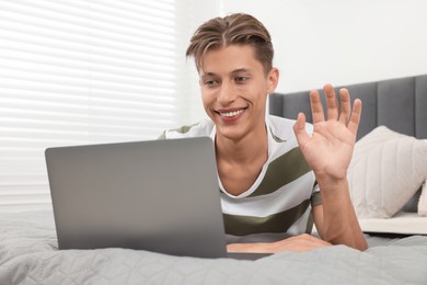 Happy young man having video chat via laptop on bed indoors