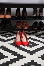 Photo of Stylish red female shoes near shelving unit in hall