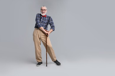 Senior man with walking cane on gray background