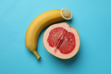 Photo of Banana with condom and half of grapefruit on light blue background, flat lay. Safe sex concept