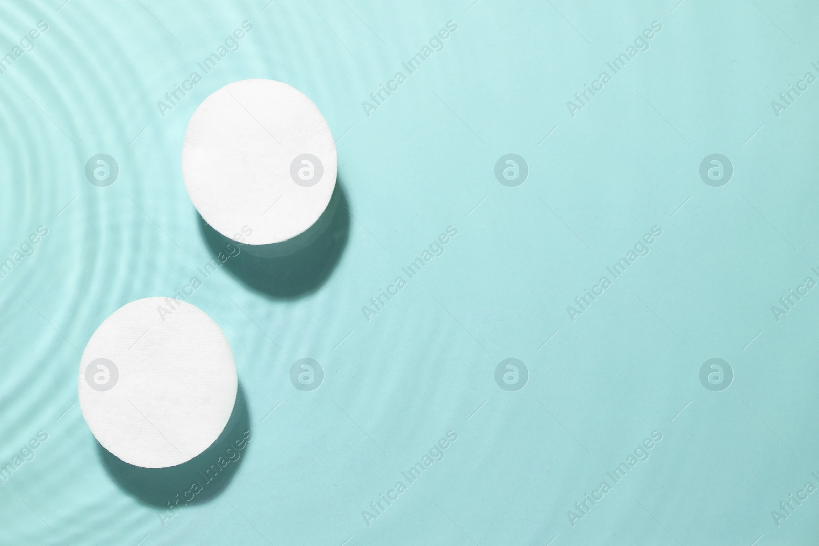 Image of Cotton pads in micellar water on light blue background, top view. Space for text