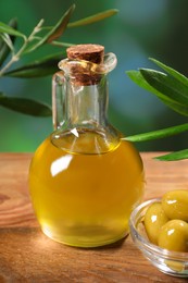 Photo of Jug of cooking oil, olives and green leaves on wooden table