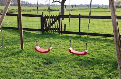 Photo of Outdoor swings on green grass near wooden fence outdoors