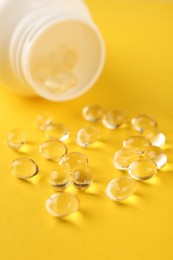 Photo of Vitamin capsules and medical bottle on yellow background, closeup