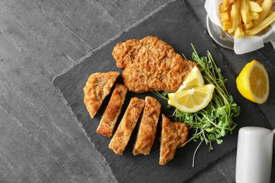 Photo of Tasty schnitzels served with french fries, microgreens and lemon on grey table, flat lay