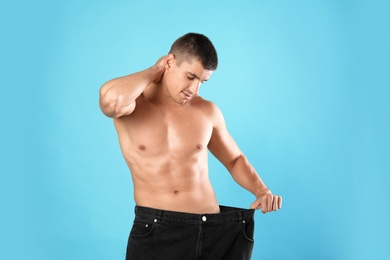 Photo of Young man with slim body in old big size jeans on light blue background
