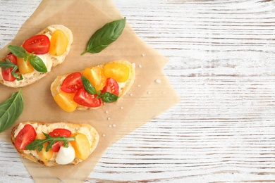 Delicious tomato bruschettas on white wooden background, top view. Space for text