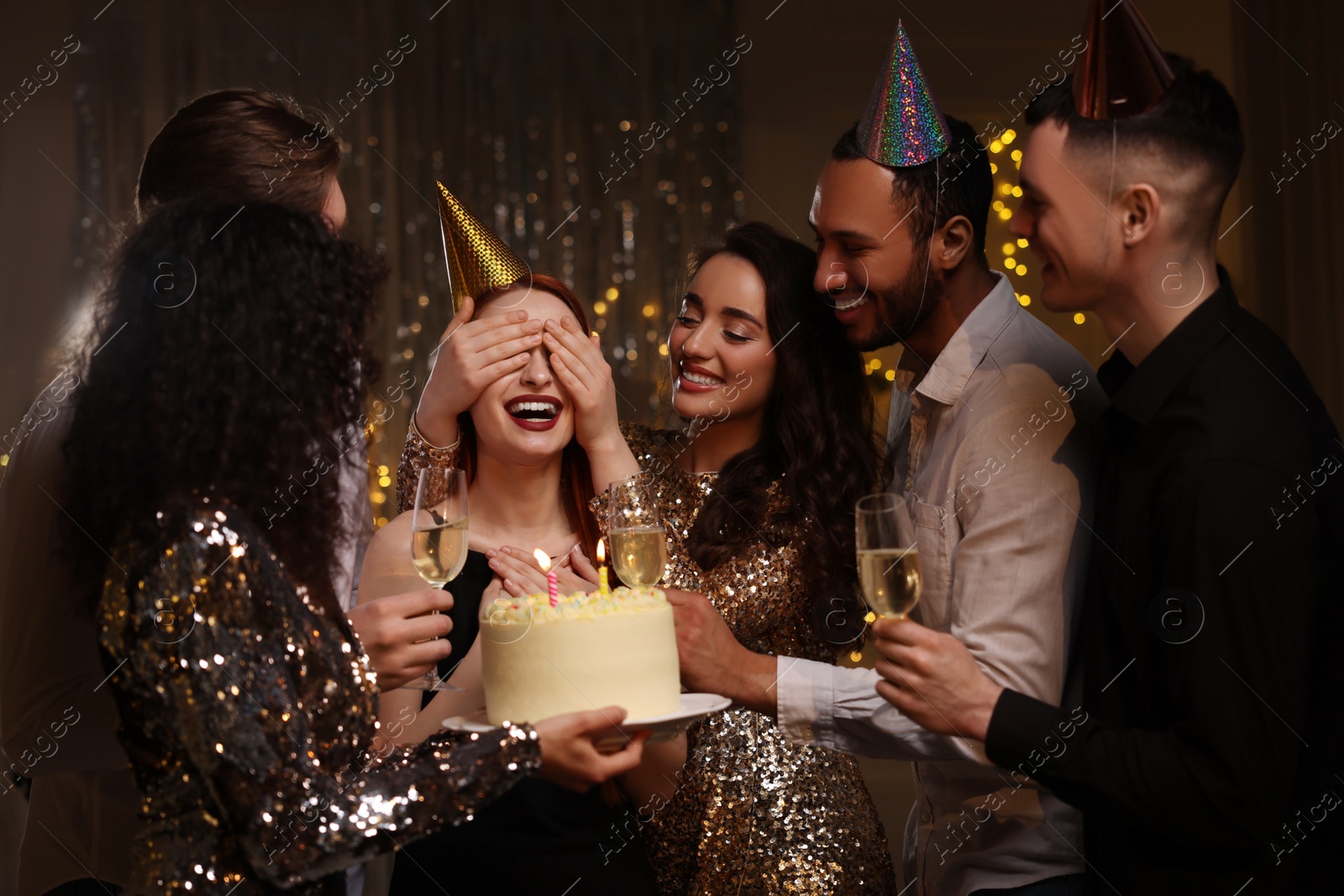 Photo of Happy friends with tasty cake and glasses of sparkling wine celebrating birthday indoors