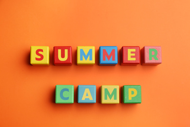 Colorful wooden cubes with phrase SUMMER CAMP on orange background, flat lay
