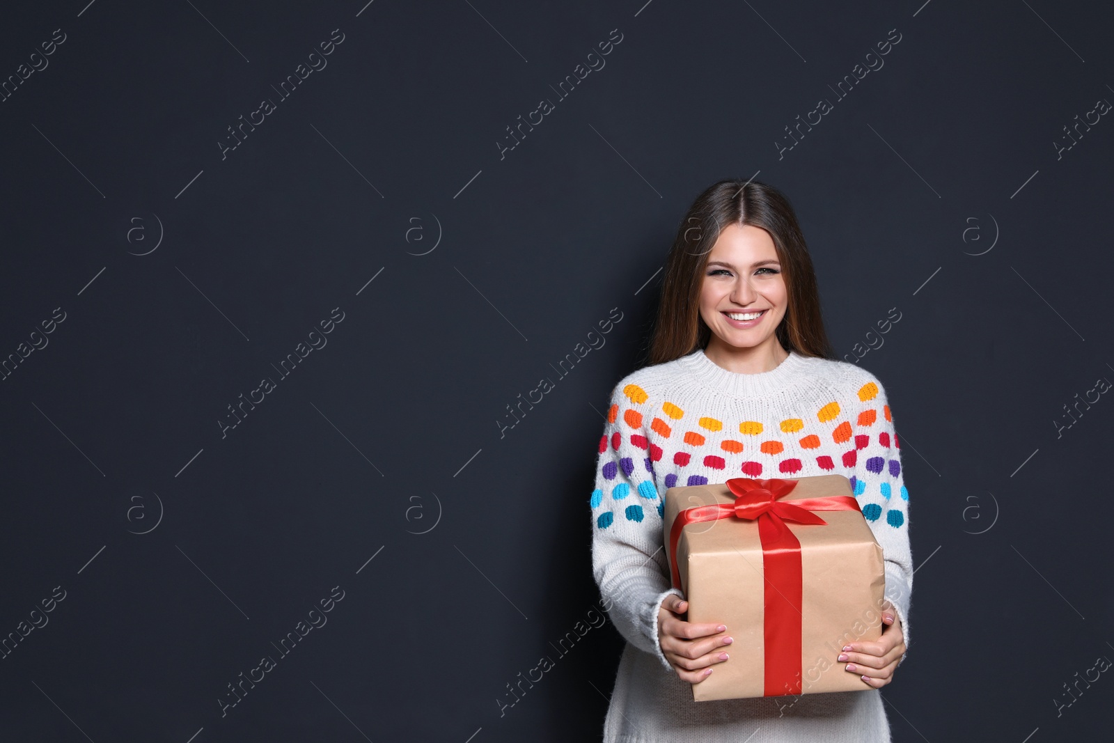 Photo of Young woman with Christmas gift on dark background. Space for text