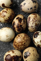 Photo of Many speckled quail eggs on black textured table, flat lay