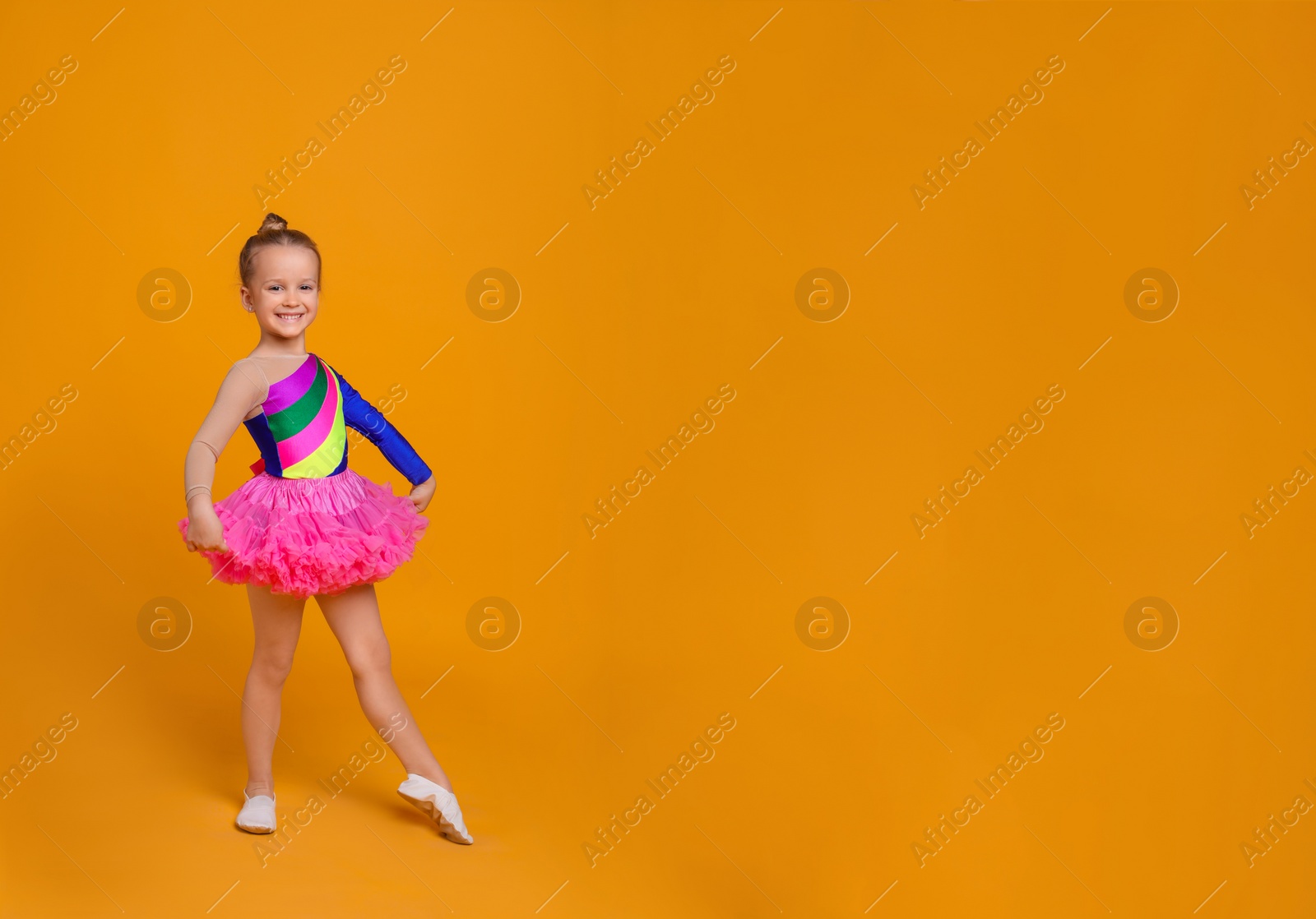 Photo of Cute little girl in costume dancing on orange background. Space for text